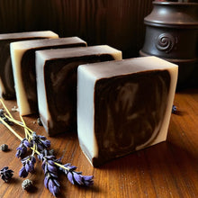 Load image into Gallery viewer, Three bars of soap with a marbled pattern on a wooden surface, accompanied by lavender flowers.