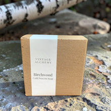 Load image into Gallery viewer, Birchwood cold process soap in a kraft paper gift box with minimalist label displayed on weathered stone with a soft-focus birch branch