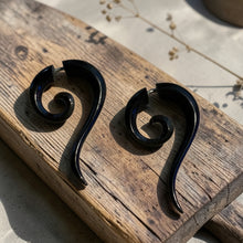 Load image into Gallery viewer, Black spiral fake gauge tribal earrings displayed on weathered wood block with soft botanical background in natural light