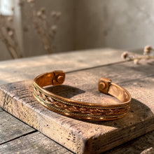Load image into Gallery viewer, Boho copper and brass cuff bracelet with braided detail displayed on weathered wood block in natural light with soft botanical background