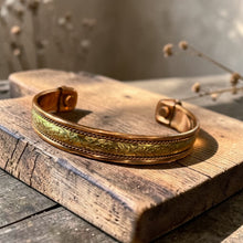 Load image into Gallery viewer, Boho etched brass and copper cuff bracelet displayed on weathered wood block with soft botanical background in natural light