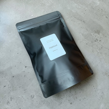 Load image into Gallery viewer, Highland loose leaf herbal tea packaged in a matte black resealable pouch displayed on a neutral stone surface.