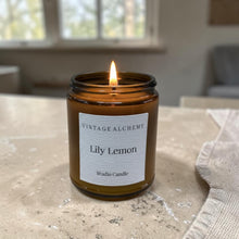Load image into Gallery viewer, Lily Lemon studio candle in amber glass jar with black lid on warm stone countertop in softly lit farmhouse kitchen setting
