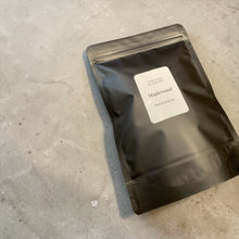 Load image into Gallery viewer, Maplewood loose-leaf black and green tea in a matte black resealable pouch displayed on a neutral stone surface.