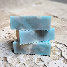 Load image into Gallery viewer, Stacked blue and gray glycerin soap bars with mineral marbling on a weathered plaster surface in a refined coastal apothecary style