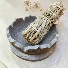 Load image into Gallery viewer, Stone lotus smudge bowl holding bundled sage on neutral mineral surface with botanical background