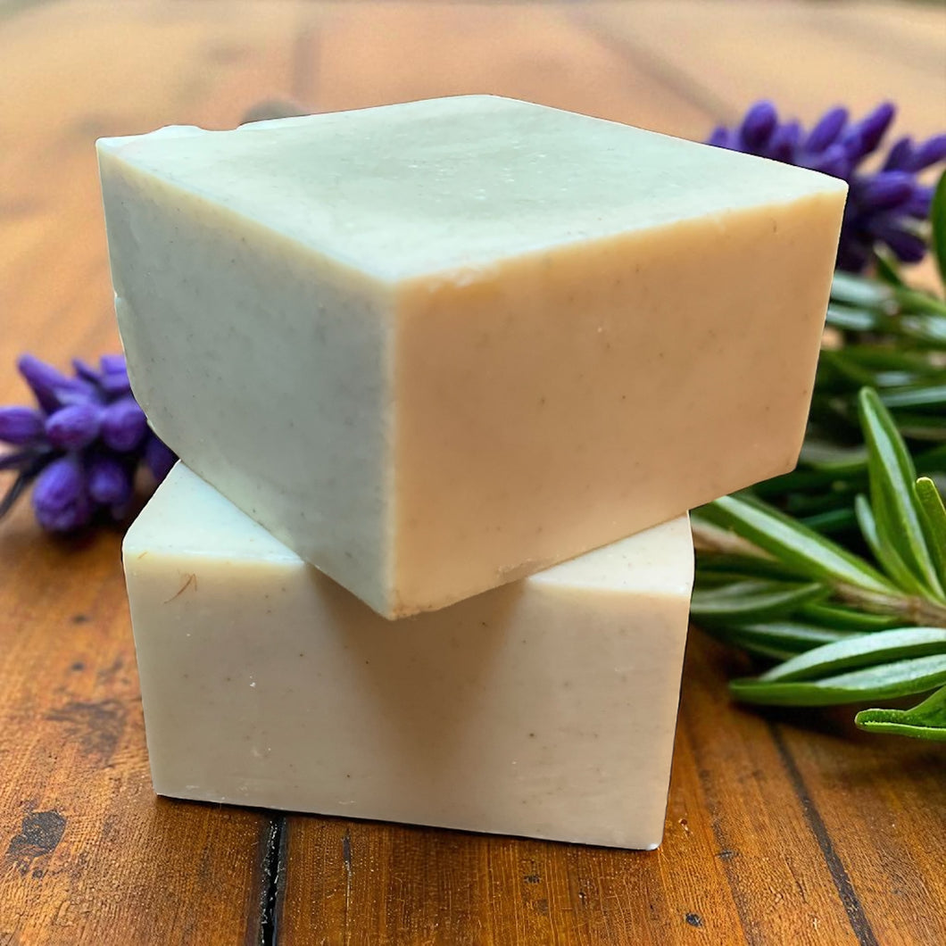 Two stacked soap bars on a wooden surface with lavender and rosemary leaves.