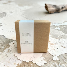 Load image into Gallery viewer, Bali cold process soap in minimalist kraft packaging displayed on a weathered plaster surface with driftwood accents

