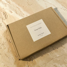Load image into Gallery viewer, Bamboo soap dish packaged in kraft box with Vintage Alchemy label on natural mineral surface
