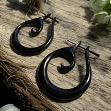 Load image into Gallery viewer, Black hoop earrings on a wooden surface with flowers in the background
