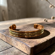 Load image into Gallery viewer, Boho brass and copper cuff bracelet with decorative pattern displayed on weathered wood block with soft botanical background in natural light
