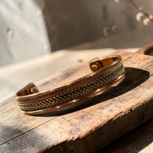 Load image into Gallery viewer, Boho brass cuff bracelet with textured pattern displayed on weathered wood block in natural light with soft botanical background
