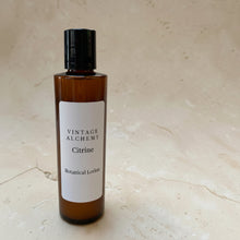 Load image into Gallery viewer, Vintage Alchemy Citrine Botanical Lotion in amber bottle on warm neutral stone background
