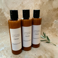Load image into Gallery viewer, Vintage Alchemy Citrine Botanical Lotion in amber bottles on warm stone surface with botanical styling
