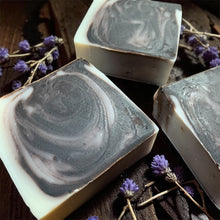 Load image into Gallery viewer, Three bars of soap with a marbled design on a wooden surface with lavender flowers.
