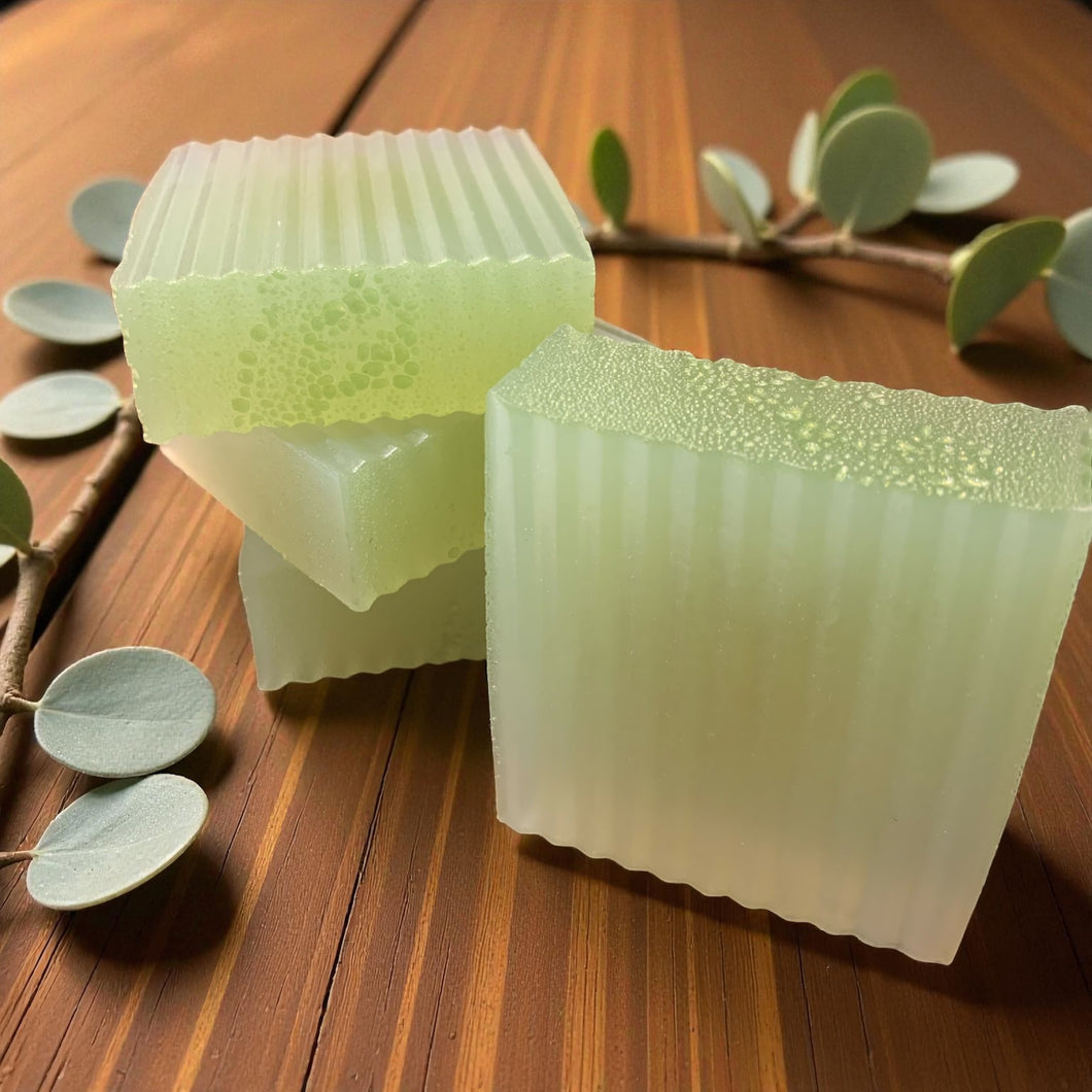 Two green soap bars on a wooden surface with leaves in the background