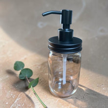Load image into Gallery viewer, amber glass pump bottle with matte black dispenser on warm stone surface with eucalyptus stem botanical studio background
