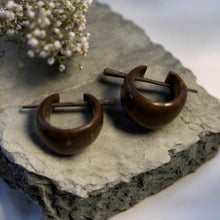 Load image into Gallery viewer, Pair of brown wood hoop earrings on a stone surface with small white flowers.
