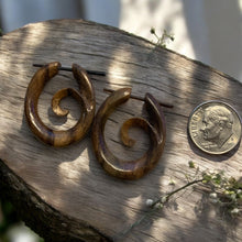 Load image into Gallery viewer, Wooden spiral earrings on a wooden surface with a coin for scale.
