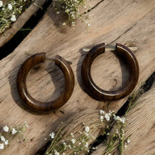 Load image into Gallery viewer, Wooden hoop earrings on a rustic wooden surface with small white flowers.
