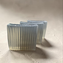 Load image into Gallery viewer, Three translucent smoky gray glycerin soap bars with ribbed texture and barbershop musk fragrance on a soft neutral stone surface.
