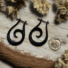 Load image into Gallery viewer, Black spiral earrings on a wooden surface with flowers and a coin for scale.
