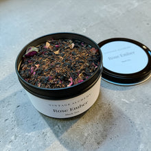 Load image into Gallery viewer, Open tin of Rose Ember loose leaf black tea with rose petals and botanicals displayed on a neutral stone surface.
