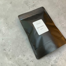 Load image into Gallery viewer, Rose Ember loose leaf black tea in a matte black resealable pouch on a neutral stone surface.
