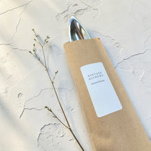 Load image into Gallery viewer, silver metal incense burner partially wrapped in kraft sleeve with vintage alchemy label on limewashed plaster background
