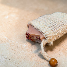 Load image into Gallery viewer, Natural sisal soap saver bag holding botanical bar soap on stone surface
