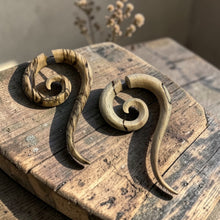 Load image into Gallery viewer, Carved spiral wood fake gauge tribal earrings displayed on weathered wood with soft botanical background in natural light
