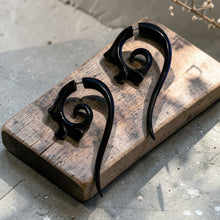 Load image into Gallery viewer, Hand-carved spiral wood tribal earrings displayed on a weathered wood block with soft botanical background in natural light
