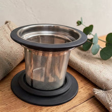 Load image into Gallery viewer, Stainless steel tea filter with black base on a wooden surface with burlap and greenery.
