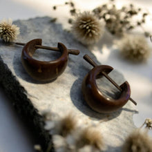 Load image into Gallery viewer, Pair of brown wood hoop earrings on a textured surface with dried flowers in the background

