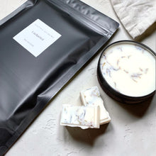 Load image into Gallery viewer, Matte black wax melt refill pouch with botanical soy wax melts and reusable apothecary wax melt dish styled on soft neutral plaster surface for Vintage Alchemy Uncharted fragrance.
