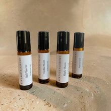 Load image into Gallery viewer, Four amber glass perfume oil roller bottles from Vintage Alchemy on a warm stone surface featuring Bali Breeze, Orchid Moon, Black Thorn, and Amber Veil fragrances.

