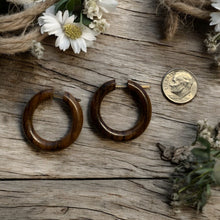 Load image into Gallery viewer, Wooden hoop earrings on a wooden surface with a coin for scale.
