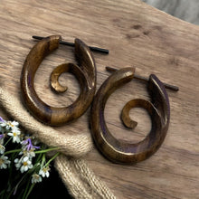 Load image into Gallery viewer, Wooden spiral earrings on a wooden surface with flowers in the background

