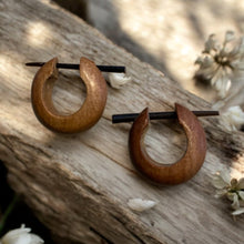 Load image into Gallery viewer, Wooden hoop earrings on a wooden surface with blurred flowers in the background
